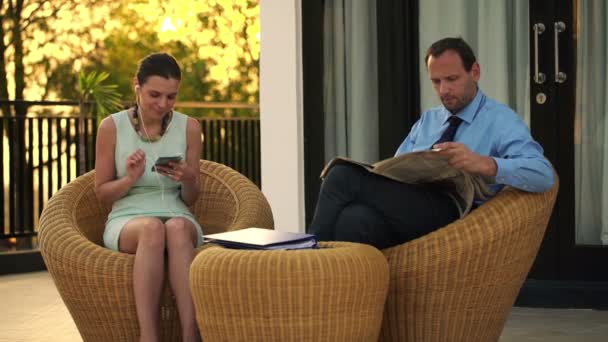 Business couple listening to music and reading newspaper — Stock Video