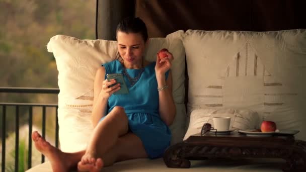 Vrouw met behulp van smartphone en eten apple — Stockvideo