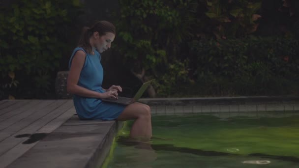 Frau arbeitet mit Laptop am Schwimmbadrand — Stockvideo