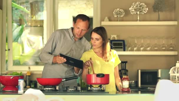 Couple using tablet and cooking in kitchen — Stock Video