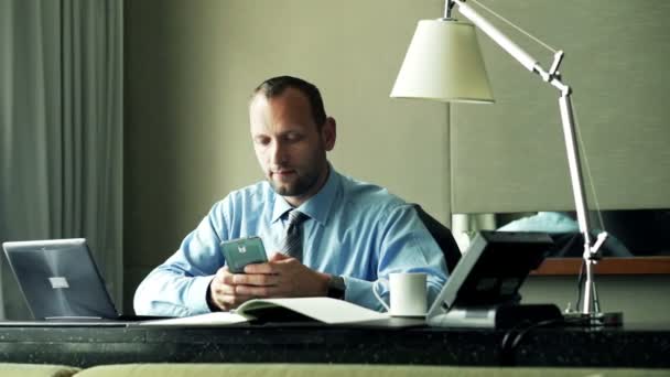 Бизнесмен использует смартфон, сидя за столом — стоковое видео