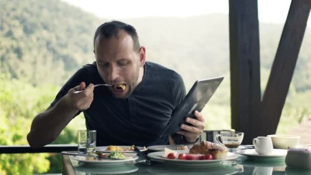 Ο άνθρωπος, ανάγνωση ειδήσεων στον υπολογιστή tablet και διατροφή πρωινό — Αρχείο Βίντεο