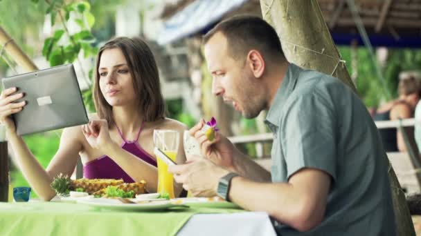 Casal com computador tablet e smartphone durante a refeição — Vídeo de Stock