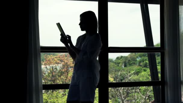 Женщина с помощью планшетного компьютера, стоящего у окна — стоковое видео