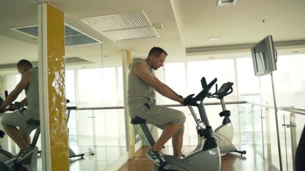 Hombre a caballo bicicleta estacionaria en el gimnasio — Vídeo de stock