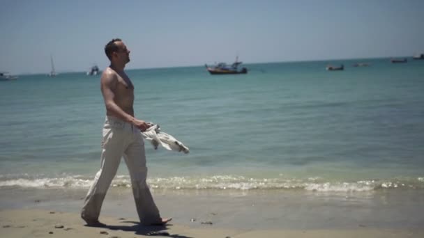 Young man in trousers walking on beach — Stock Video