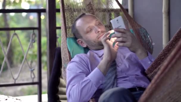 Бизнесмен использует смартфон на гамаке — стоковое видео