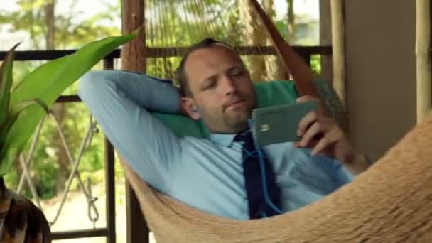 Hombre de negocios viendo la película en el teléfono inteligente en hamaca — Vídeo de stock