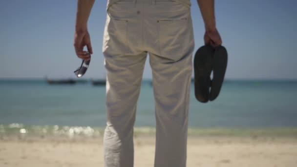 Hombre con sandalias y gafas de sol de pie en la playa — Vídeo de stock