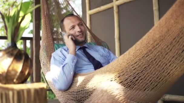 Joven hombre de negocios hablando por celular en hamaca — Vídeo de stock