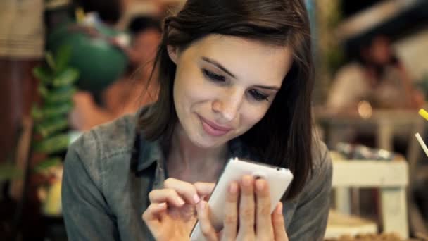 Mujer joven con teléfono inteligente sentado en la cafetería — Vídeos de Stock