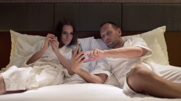 Pareja hablando y usando smartphone en la cama — Vídeos de Stock