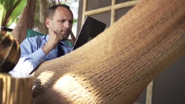 Podnikatel s počítačem tablet ležící na houpací síť — Stock video