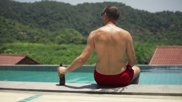 Giovane uomo rilassante con birra a bordo piscina — Video Stock