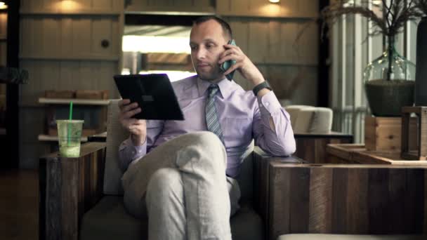 カフェで携帯電話で話しているタブレット コンピューターを持ったビジネスマン — ストック動画