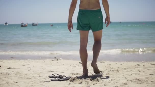 Man kastar floppen-flops på sand och gå in i havet — Stockvideo