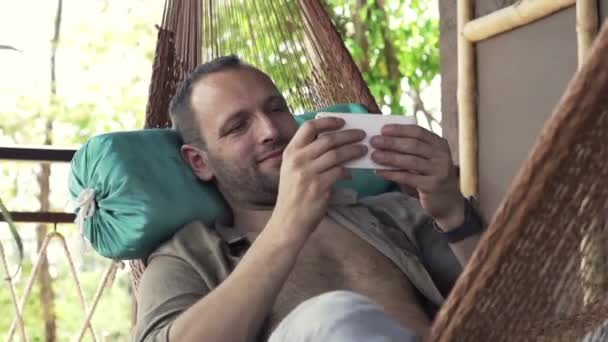 Человек играет в игру на смартфоне на гамаке — стоковое видео