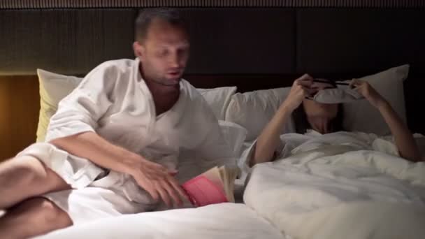 Para całuje i człowiek, czytanie książki w łóżku — Wideo stockowe