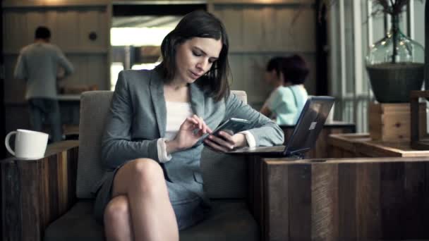 Affärskvinna med smartphone och laptop sitter i café — Stockvideo