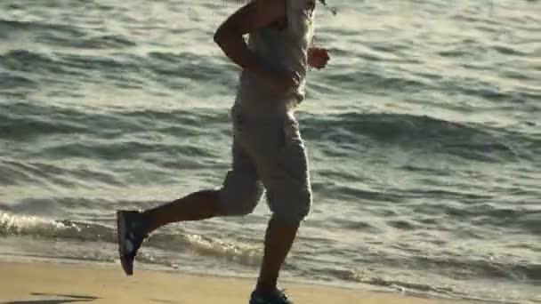 Молодой человек бегает по пляжу — стоковое видео