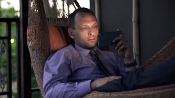 Geschäftsmann schaut Film auf Smartphone in Hängematte — Stockvideo