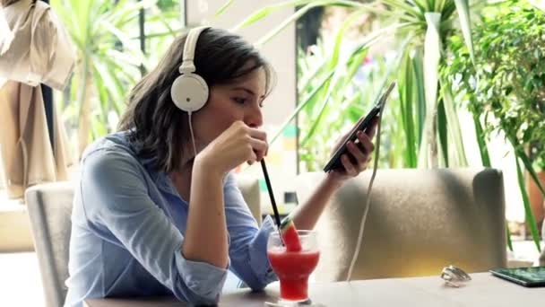 Vrouw luisteren naar muziek op mobiel en drinken cocktail — Stockvideo