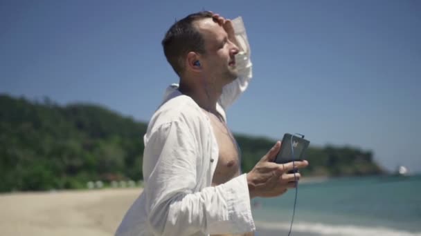 Člověk poslouchá hudbu na mobil a tančí na pláži — Stock video