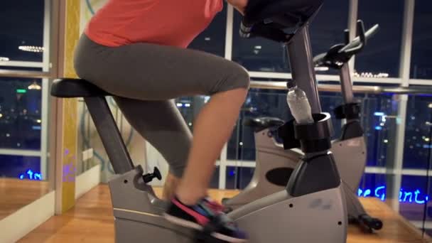 Piernas de mujer en bicicleta estacionaria en el gimnasio — Vídeo de stock