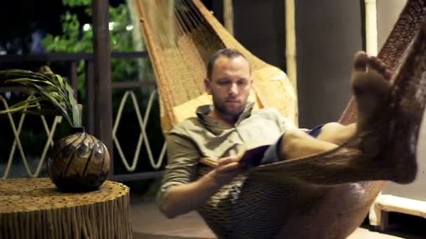 Homem lendo livro deitado na rede — Vídeo de Stock