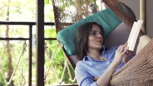 Mujer leyendo libro acostado en la hamaca en la terraza — Vídeo de stock