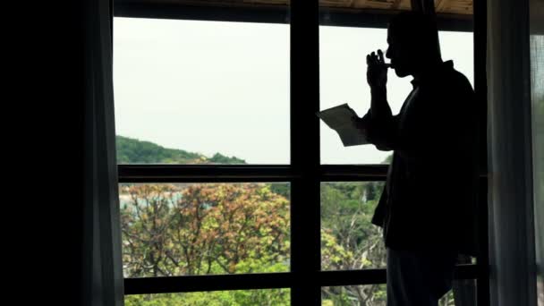 Hombre leyendo periódicos y bebiendo por la ventana — Vídeo de stock