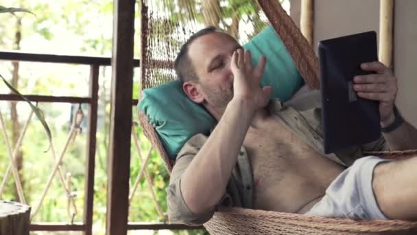 Man chatting on tablet computer lying on hammock — Stock Video