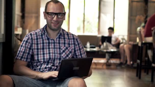 Muž s notebookem, mluví do kamery v kavárně — Stock video