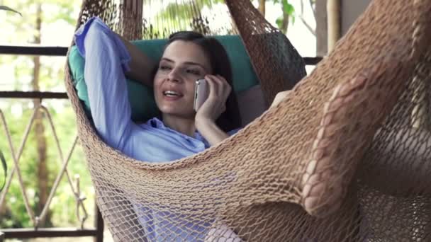 Femeie vorbind pe telefonul mobil în timp ce stătea întinsă pe hamac — Videoclip de stoc