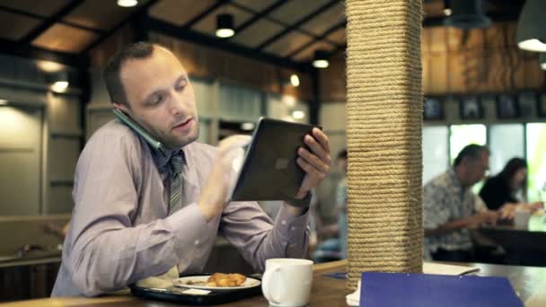 Uomo d'affari con tablet che parla al cellulare nel caffè — Video Stock