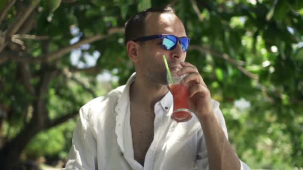 Людина п'є тропічний коктейль в парку — стокове відео