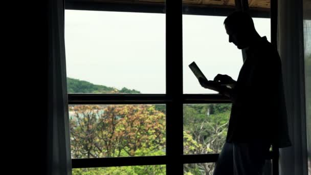 Hombre usando el ordenador portátil de pie por ventana — Vídeos de Stock