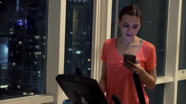 Woman with smartphone exercising on elliptical machine — Stock Video