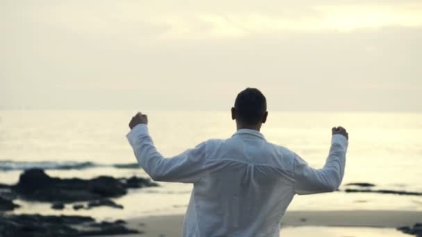 Homem levantando braços para o céu em pé na praia — Vídeo de Stock