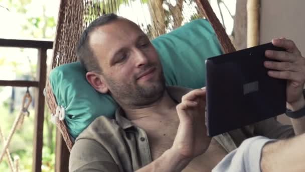 Hombre usando la computadora de la tableta mientras que miente en hamaca — Vídeo de stock