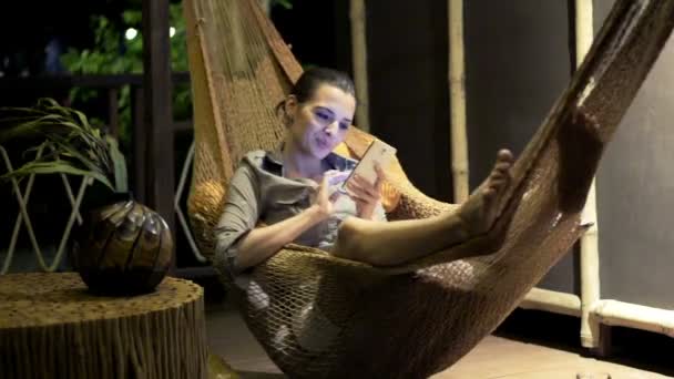 Young woman with smartphone lying on hammock — Stock Video