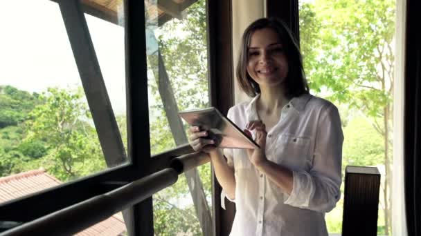 Mujer con tablet ordenador de pie por la ventana — Vídeos de Stock