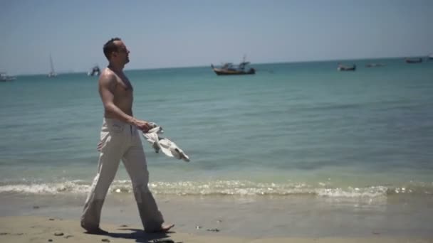 Young man in trousers walking on beach — Stock Video