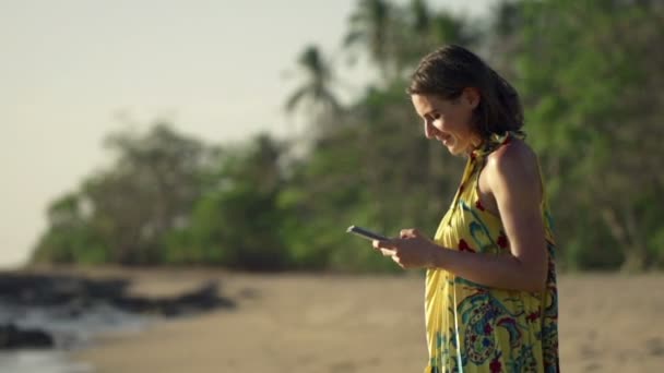 Молодая женщина со смартфоном прогуливается по пляжу — стоковое видео