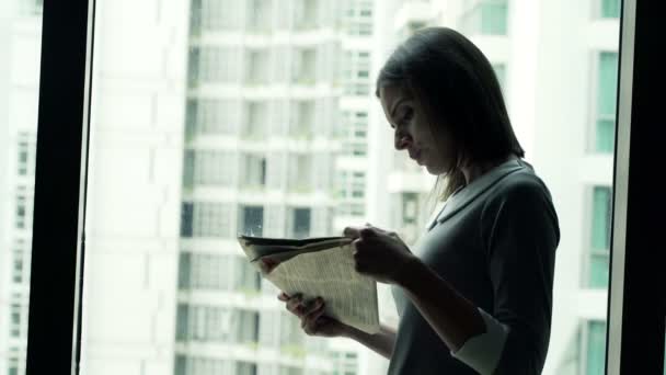 Business woman reading newspaper while standing by window — стоковое видео