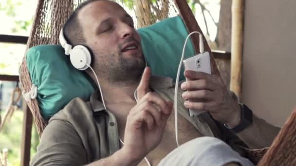Man listening music and singing on hammock — Stock Video