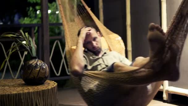 Несчастный человек лежит на гамаке ночью — стоковое видео