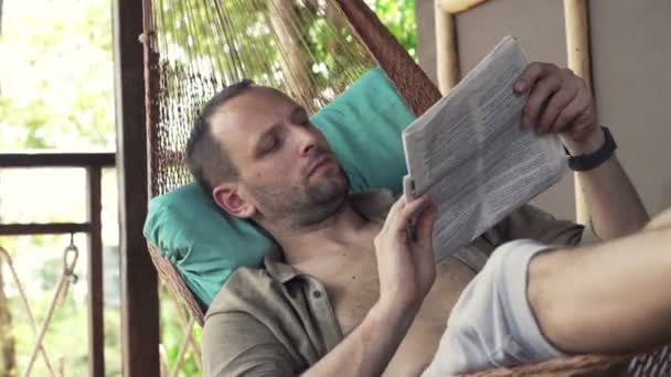 Mann liest Zeitung in Hängematte auf Terrasse — Stockvideo