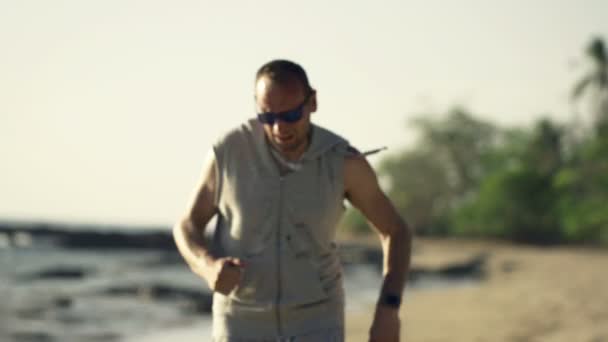 Мужчина бегает по пляжу и берет перерыв — стоковое видео