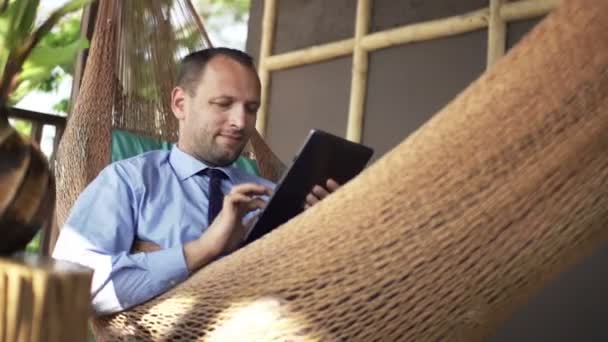 Hombre de negocios con la computadora de la tableta que miente en hamaca — Vídeos de Stock